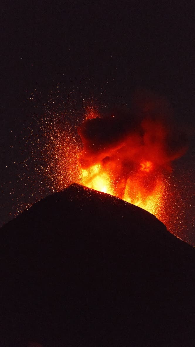 A volcano erupting at night, lava and embers against black sky