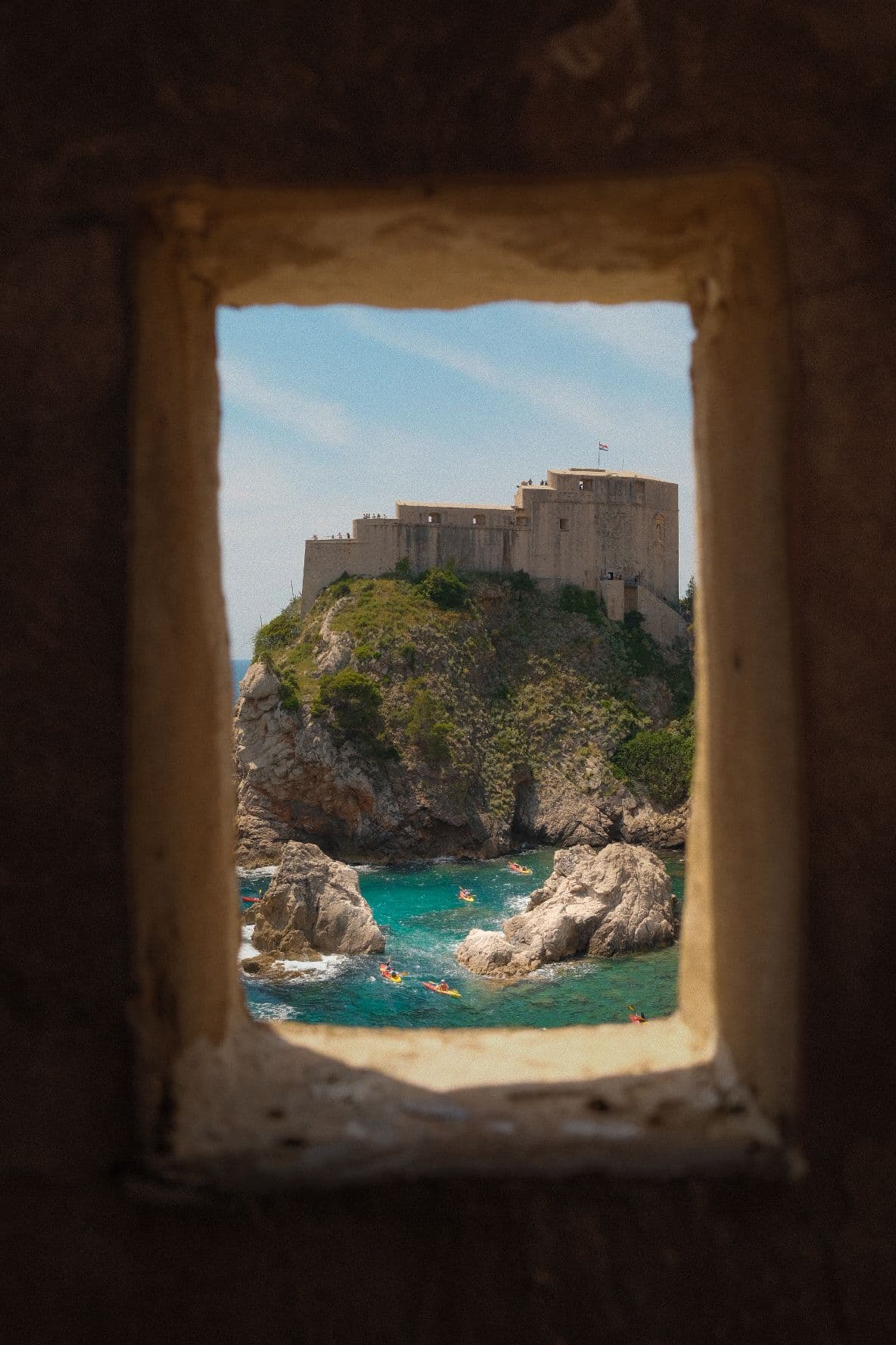 Dubrovnik's Fort Lovrijenac framed through a stone window, kayaks below