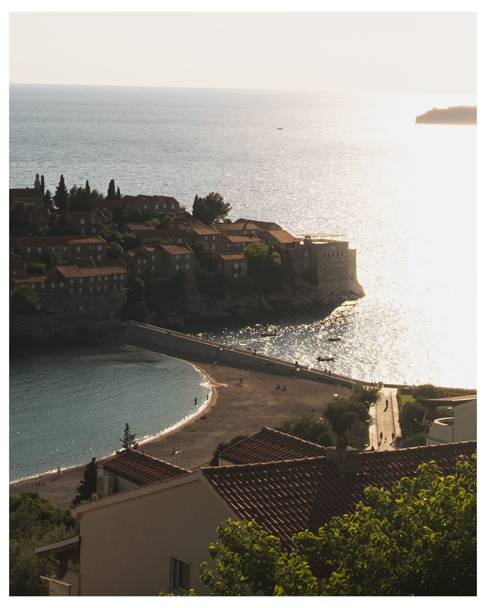 Aerial view of Sveti Stefan's beach and rooftops at golden hour, Montenegro